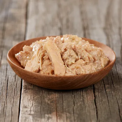 Nahaufnahme von zerkleinertem, saftigem Fleisch in einer Holzschale auf einem Holztisch. Produktdarstellung für Tiernahrung.