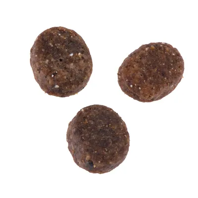 Tre brune, ovale foderpiller med synlige korn og små hvide stykker. Ingen mærkning eller emballage synlig.