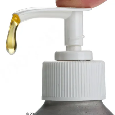 Närbild av en pumpdispenser med en droppe gulaktig vätska som kommer ut.