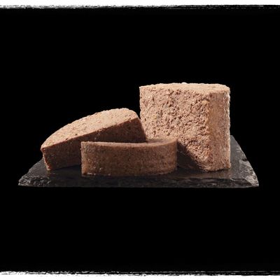 Comida húmida para animais de estimação em formato de patê, cortada em fatias grossas e apresentada sobre uma base escura. Sem embalagem visível ou marcas identificáveis.