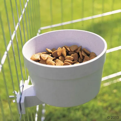 Ciotola per alimenti in plastica fissata a una griglia metallica, riempita con crocchette marroni. Adatta per recinti con griglia all'aperto.