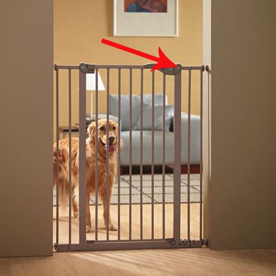 Puerta de seguridad metálica instalada en un marco de puerta, con flecha roja señalando el mecanismo de cierre. Perro grande detrás de la barrera.