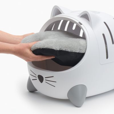 Handen plaatsen een grijs, zacht kussen in een witte kattenhuisje met oren- en pootjesdesign.