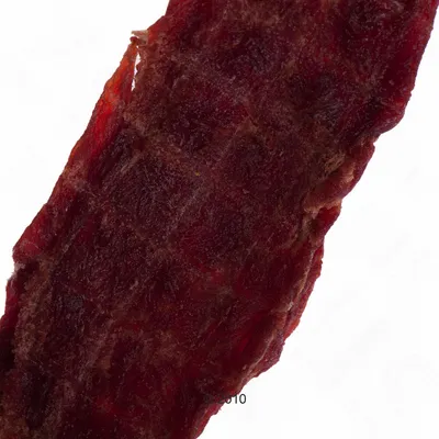 Zbliżenie na czerwony, suszony pasek mięsa. Struktura i kolor produktu są wyraźnie widoczne.