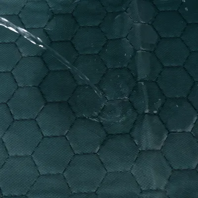 Jet d’eau versé sur un tissu à motif hexagonal, surface en textile visible, couleur foncée. Aucun logo ni texte apparent.