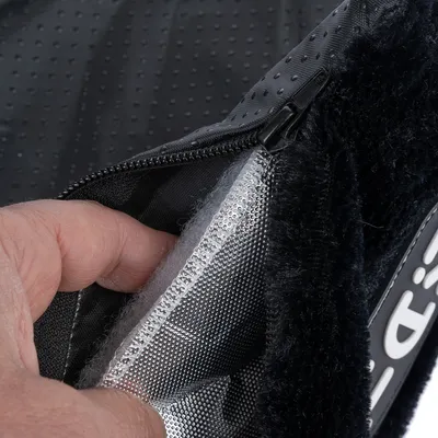 Gros plan sur une main ouvrant une fermeture éclair d’un coussin pour animaux, montrant l’intérieur en tissu, rembourrage blanc et surface extérieure noire à pois antidérapants.