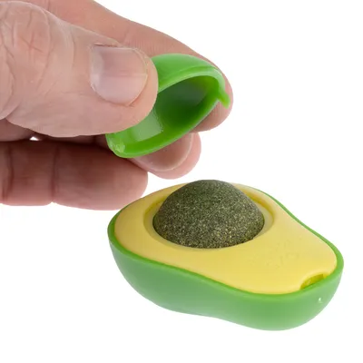 Hånd åbner grønt og gult avocadoformet kattelegetøj med aftagelig kugle af presset materiale.