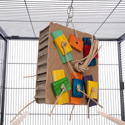 Papierowa zabawka z kolorowymi drewnianymi elementami i sznurkami, zawieszona na metalowym łańcuchu w klatce.