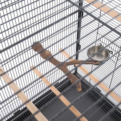 Interno di gabbia per uccelli con posatoi in legno, ramo naturale e ciotola per mangime in acciaio inox.