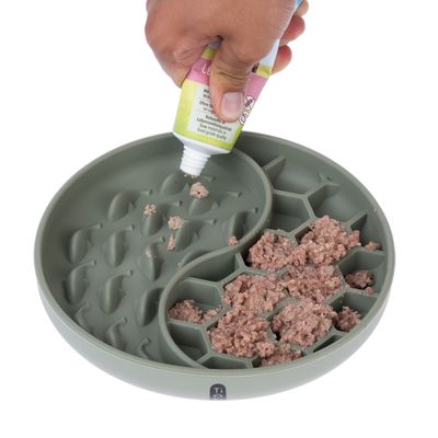 Grön matskål med strukturerad yta, fylld med våtfoder. Hand pressar tub med pastaliknande innehåll i skålen.