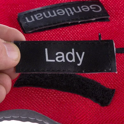 Svart kardborreetikett med vit text "Lady", bredvid en annan etikett med texten "Gentleman" på röd tygbakgrund.