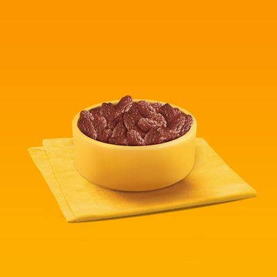 Bowl filled with brown, dry pet food pieces placed on a yellow cloth against an orange background.