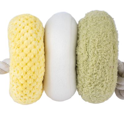Jouet pour chien composé de trois anneaux en tissu jaune, blanc et vert clair à textures différentes, reliés par une corde épaisse en coton beige visible sur les côtés.