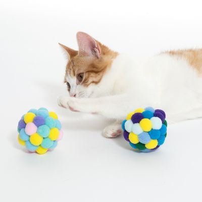 Gatto che gioca con palline colorate di morbidi pompon in tessuto. Il prodotto mostra un gioco per gatti.