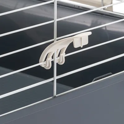Close-up of a white plastic clip for attachment to metal bars, part of a grey enclosure.