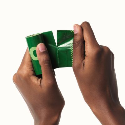 Deux mains détachent un sac vert d’un rouleau de sacs en plastique, texte partiel « O » visible sur l’emballage.