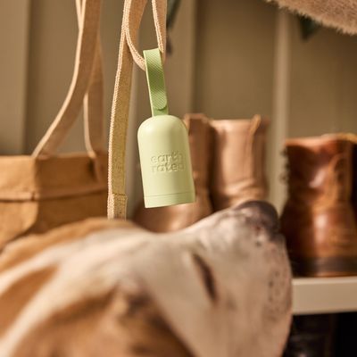 Distributeur vert avec texte visible « earth rated » accroché à une sangle, devant des sacs et des bottes en arrière-plan.