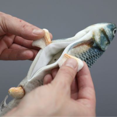 Рука открывает молнию на игрушке в форме рыбы, показывает внутренний карман для аксессуаров или наполнителя.