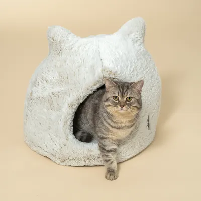 Grijze kat zit in een wit, pluizig kattenhuis met oordesign en ronde ingang.