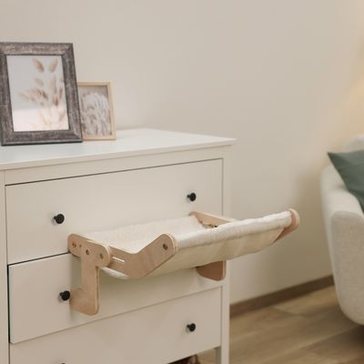 Houten hangmat met zachte vulling, gemonteerd op een witte commode. Geschikt voor kleine huisdieren of decoratie.