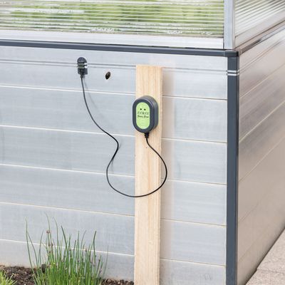 Dispozitiv electronic de protecție împotriva melcilor Snail Stop, montat pe un stâlp de lemn lângă o seră. Cablu și senzor vizibile.