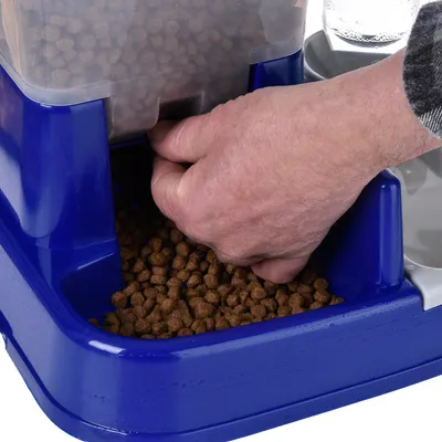Mano che preleva cibo secco da un distributore di cibo blu con contenitore trasparente.