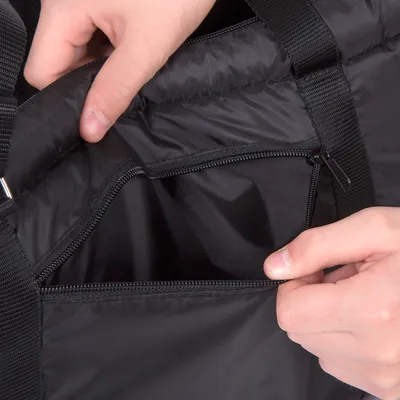 Primo piano di una borsa nera con cerniera, aperta da una mano. Mostra la tasca interna e i dettagli del materiale.