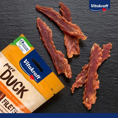 Vitakraft pure Duck Filets, korn- og tilsætningsstoffri, genanvendelig emballage. Tre andefiletsstrimler synlige ved siden af produktets emballage.