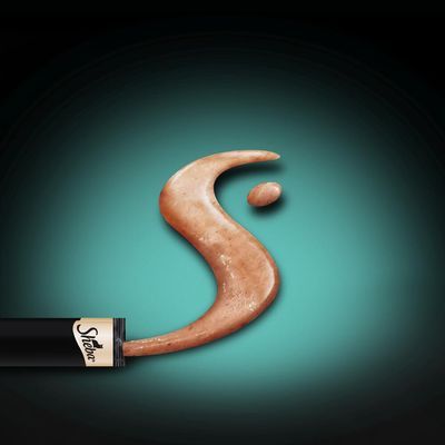 Uitgeknepen tube met zichtbaar merk Sheba, bruine pasta in S-vorm op een groene achtergrond.