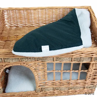 Panier en osier à deux niveaux avec coussins amovibles en tissu polaire blanc et étiquette d’entretien visible sur le dessus.