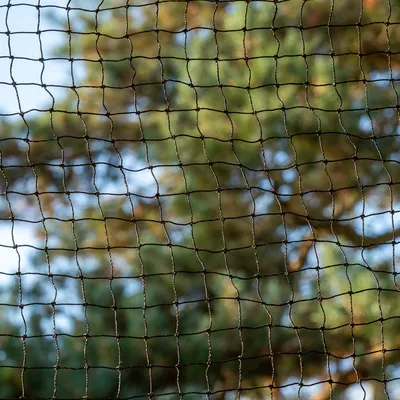 Gros plan sur un filet à mailles carrées en corde noire, fond flou avec des arbres et ciel bleu visibles à travers le filet. Matériau : corde tressée.