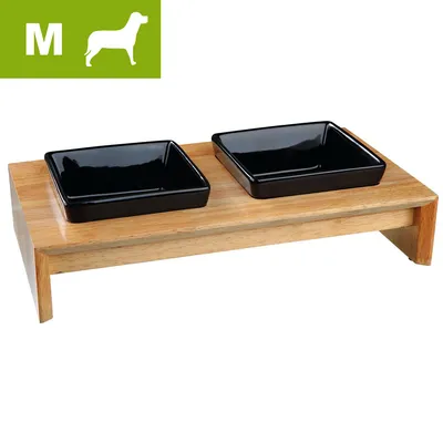 Kaksi mustaa neliönmuotoista kuppia puisella korokkeella, vasemmassa yläkulmassa vihreä laatikko, jossa valkoinen koiran siluetti ja kirjain M.