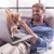 Oranje kat op laptop naast persoon op bank, merknaam Happy Cat rechtsonder zichtbaar.