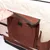Close-up of a hand opening a brown fabric pocket with a Velcro fastening on the side of a beige and brown bag, showing storage compartment detail.