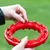 Red interactive feeding ring filled with small dry food pieces. Hands place food into the indentations of the ring.