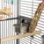 Intérieur de cage à oiseaux avec mangeoire en métal, perchoir en bois, jouet suspendu à perles colorées et bâtonnet de graines attaché aux barreaux.