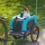 Hafenbande Fahrradanhänger in Blau mit Netzfenstern, befestigt an einem Fahrrad. Hund sitzt im Anhänger und schaut heraus.