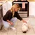 Una donna accarezza un piccolo cane bianco che mangia da una ciotola, in una cucina con piastrelle chiare e mobili bianchi. Una donna accarezza un piccolo cane bianco che mangia da una ciotola, in una cucina con piastrelle chiare e mobili bianchi.