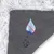 Nahaufnahme einer grauen, genoppten Unterseite mit durchgestrichenem Wassertropfen-Symbol, Hinweis auf wasserabweisende oder wasserdichte Materialeigenschaft.