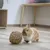 Conejo marrón junto a una pelota de material natural trenzado sobre suelo de madera. Producto para el entretenimiento de pequeños animales.