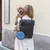 Donna con zaino nero e accessori blu, tiene un cane piccolo. Lo zaino mostra il logo 'NT'.