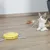 Yellow interactive cat toy with feather attachment, cat playing on wooden floor.