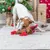 Dog playing with a brown plush toy with red details in front of a Christmas tree and presents.