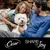 Cesar brand with the text 'Share the Joy' shown below a dog sitting between two people on a sofa outdoors.
