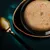 Close-up of a bowl with moist, chopped ingredients in light sauce. Golden spoon next to it on dark background.
