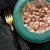 Close-up of served wet food on a green plate with a sprig of rosemary, next to a gold fork and black napkin.