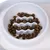 White anti-gulping bowl with wave-shaped obstacles, filled with brown dry food pieces.