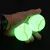 Two glowing tennis balls in a hand, suitable for playing in the dark.