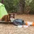 Hund liegt auf einer Matte neben Nomad Tales Decke, zwei Futterschalen und einem orangefarbenen Futterbehälter im Freien vor einem Zelt.