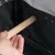 Hand toont het monteren van een houten staaf in een zwarte transportbox met netstof en metalen klinknagels.